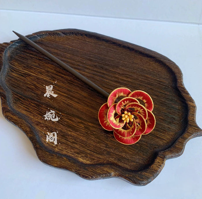 Chanhua handmade red camellia hairpin with gold edge petals and yellow stamens, displayed on a dark wood tray