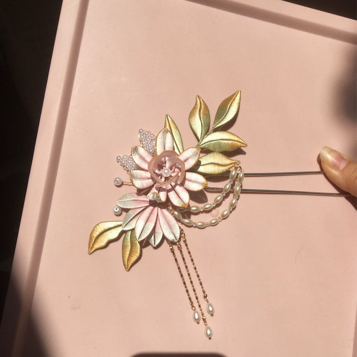 Chanhua handmade pink flower and gold leaf hairpin with pearl chain drape and drop tassels, held against a pink background