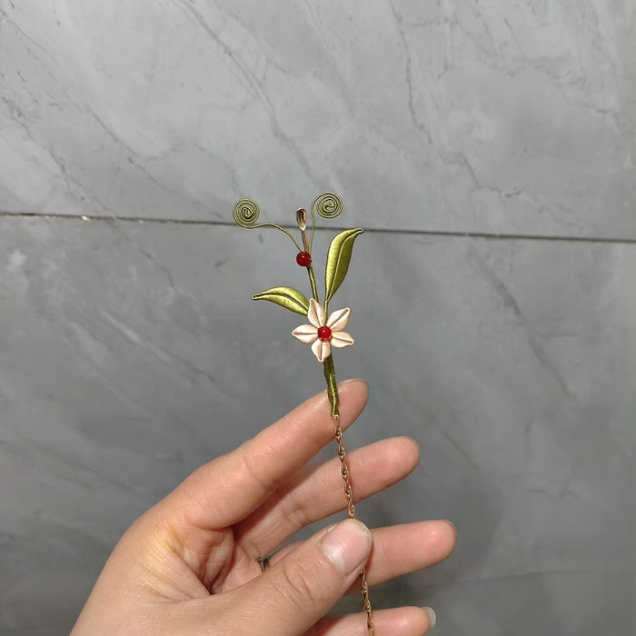 Handheld view of a handmade Chanhua thread-wrapped fairy wand hairpin with a blue spiral base, white floral center, and red bead accent.