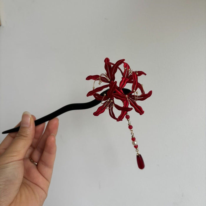 Handheld view of a handcrafted Chanhua thread-wrapped red Spider Lily hairpin with a beaded teardrop tassel.