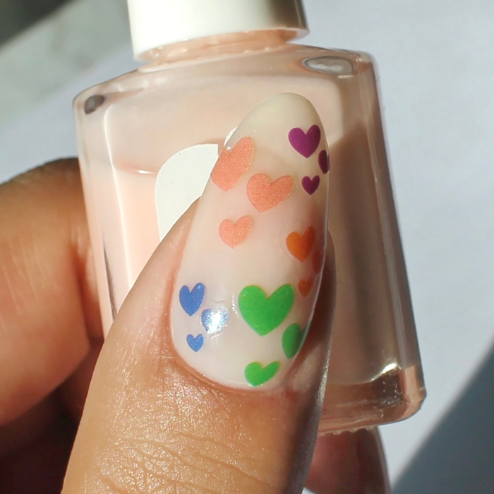 Heart on My Sleeve rainbow heart decals on a sheer nude nail, holding the bottle