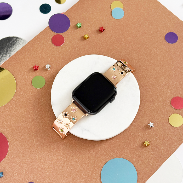 Rose gold Ibiza Coloured Stone Apple Watch strap on marble surface with scattered confetti and star shapes.