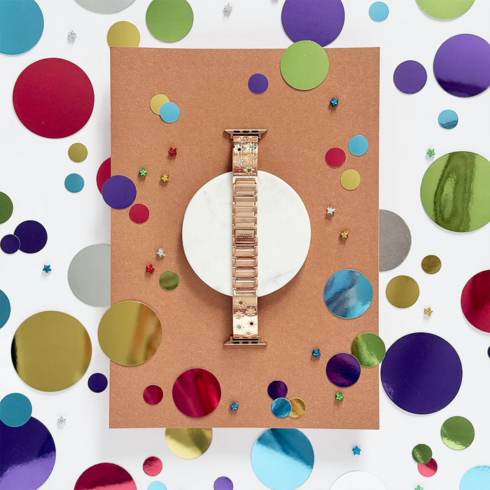 Rose gold Apple Watch strap with colorful stones by Coconut Lane, displayed on marble with confetti dots and stars.