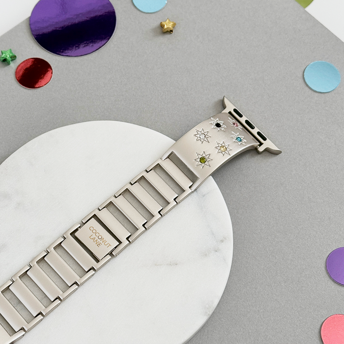 Ibiza Coloured Stone Apple Watch strap in Starlight, shown on a gray and white surface with confetti accents.