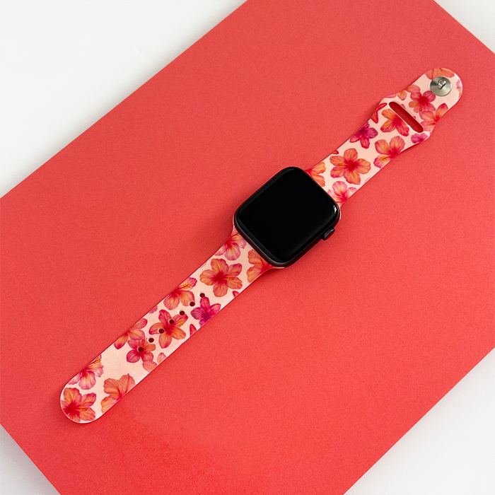 Pink hibiscus-patterned Apple Watch strap from Coconut Lane on a red rectangular surface.