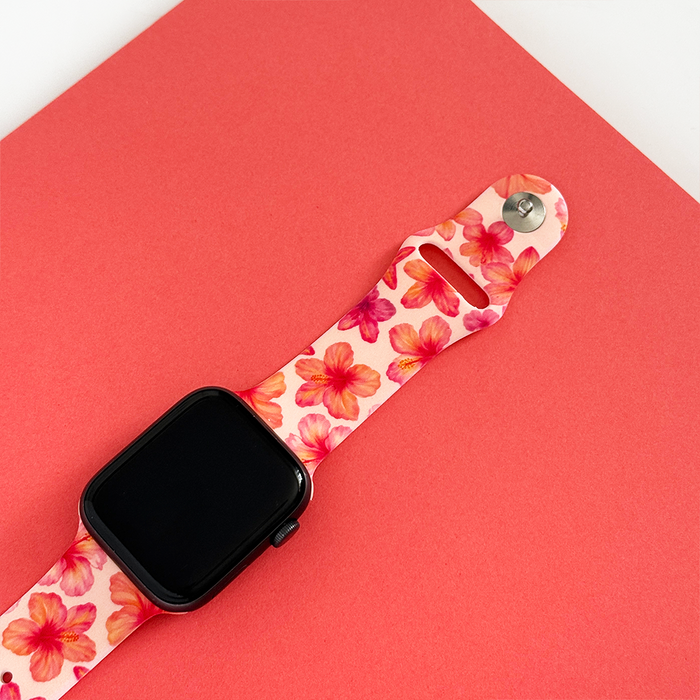 Pink hibiscus-patterned Apple Watch strap from Coconut Lane on a coral background.