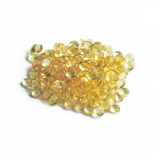 Small, round, translucent yellow capsules are scattered across a white surface, resembling fresh vitamin supplements.