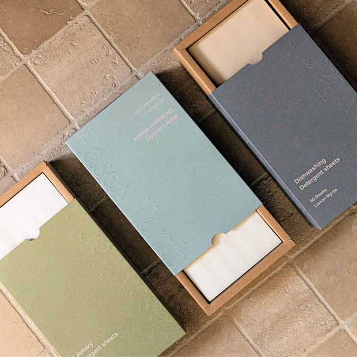Three packages of Ease.y Earth laundry & dishwashing detergent sheets on a tiled floor.