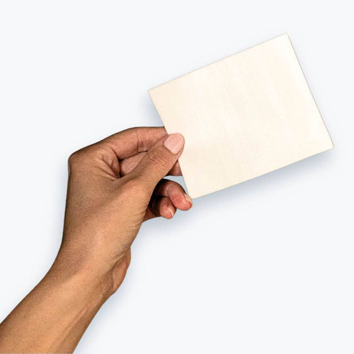 Hand holding a single laundry detergent sheet against a white background.