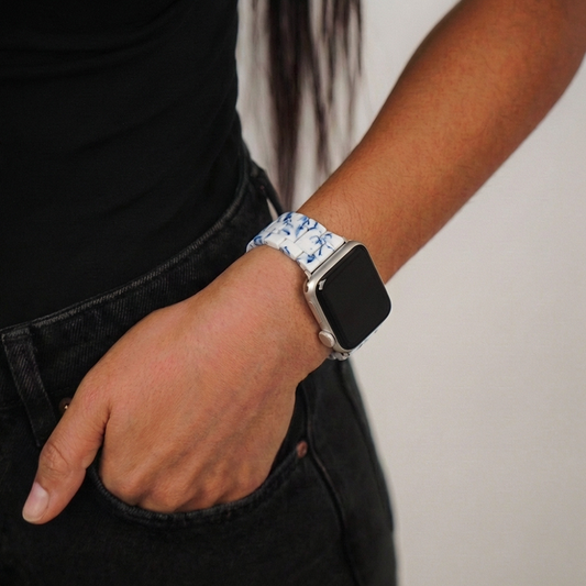 Person in black outfit wearing a blue and white Coconut Lane Apple Watch strap, hand in pocket.