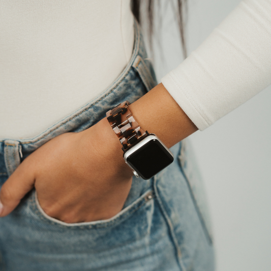 Luxe ivory tortoiseshell Apple Watch strap on wrist, hand in jeans pocket, white long-sleeve shirt shown.