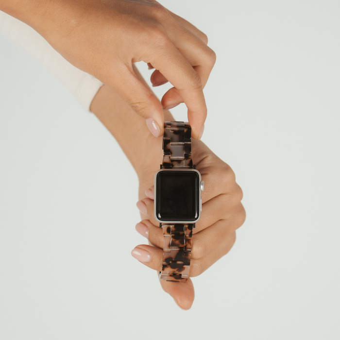 A person fastens an ivory tortoiseshell Apple Watch strap from Coconut Lane around their wrist.