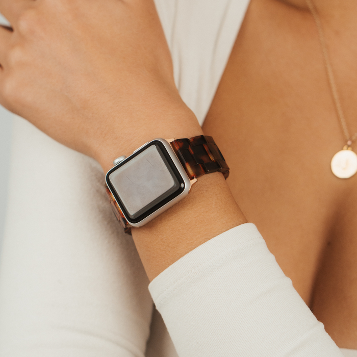Coconut Lane Luxe tortoiseshell Apple Watch strap on wrist, paired with a gold round pendant necklace.