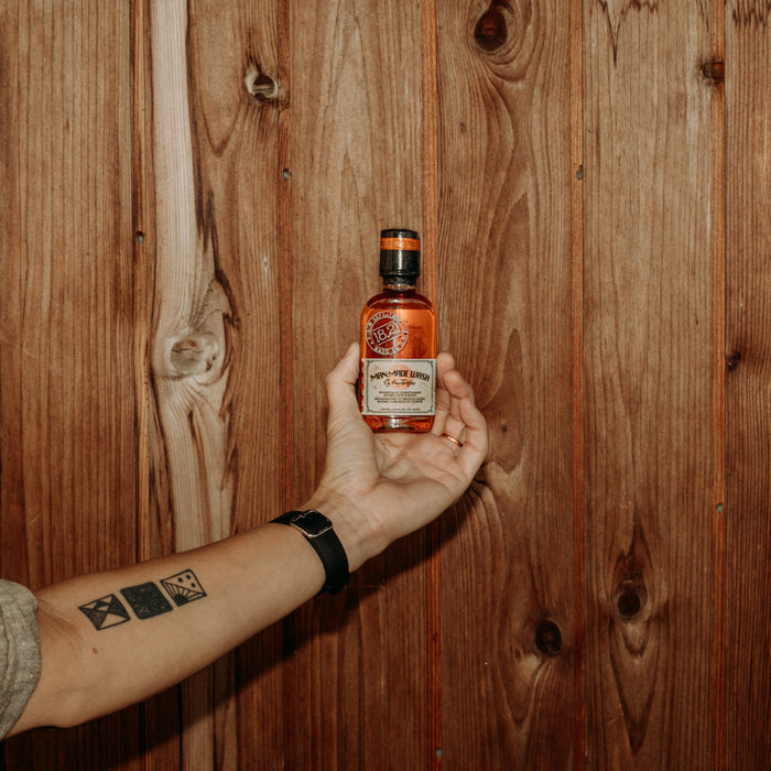 Hand holding a bottle of Man Made Wash in 3.4 oz travel size  against a wooden background