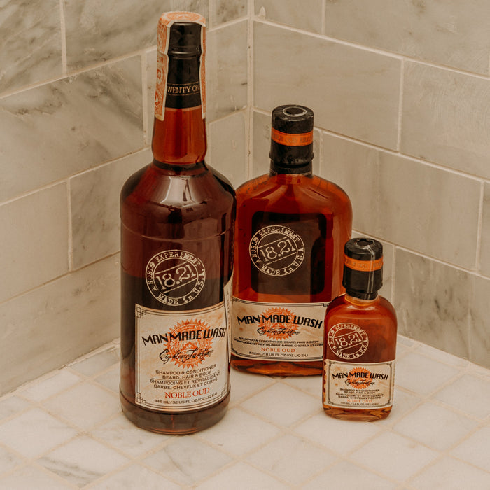 Three bottles of 1821 Man Made Washon a tiled surface with a marble wall background.