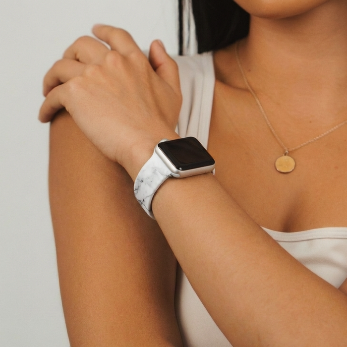 Person wearing a marble-patterned Apple Watch strap and gold necklace, hand resting near shoulder.
