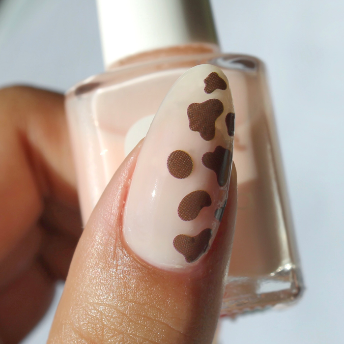 Moo-ve Over brown cow print decal on a sheer nude nail, holding the bottle