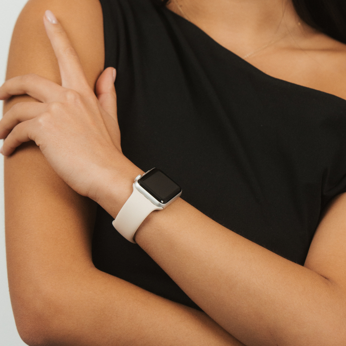 Person in black sleeveless top with arms crossed wearing Coconut Lane NAKD Apple Watch strap in almond white.