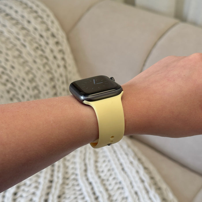 Black smartwatch with a yellow Coconut Lane NAKD Apple Watch strap, worn on a beige couch.