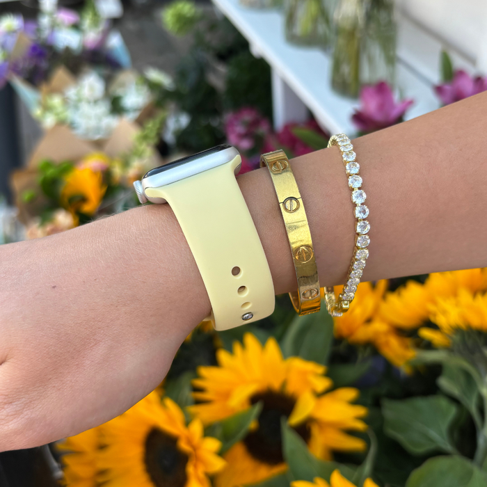 Butter yellow Coconut Lane NAKD Apple Watch strap with gold and diamond bracelets, sunflowers in the background.