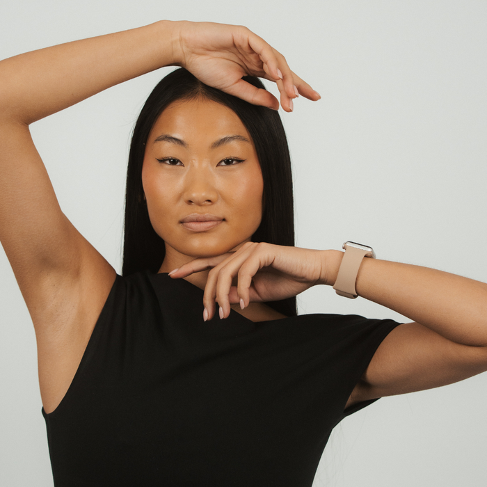 Woman in black top wearing a caramel brown Coconut Lane NAKD Apple Watch strap, plain background.