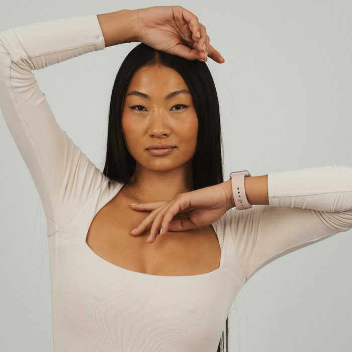 Woman with long black hair in a cream top wears a light pink Apple Watch strap by Coconut Lane.