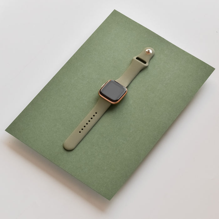 Smartwatch with a khaki Coconut Lane NAKD Fitbit strap on a green folder, set against a white background.