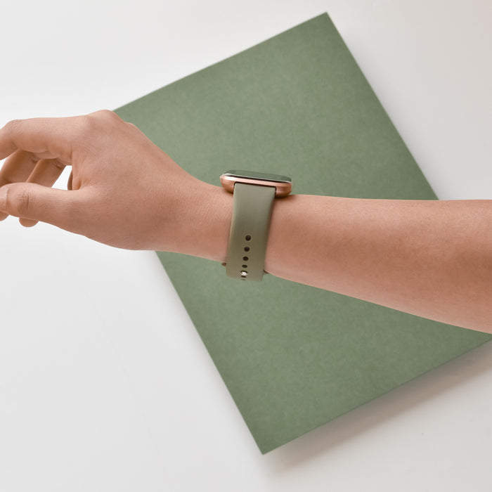 Coconut Lane NAKD Fitbit Strap in vintage khaki on a wrist, arm resting on a green notebook.