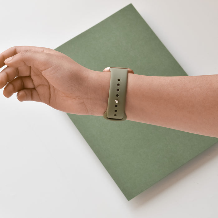 Coconut Lane NAKD Fitbit Strap in Vintage Khaki worn on a hand, resting on a green rectangular surface.