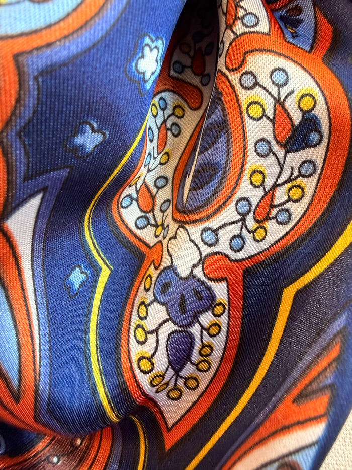 Wild rag scarf close-up with navy, orange, and white paisley pattern border