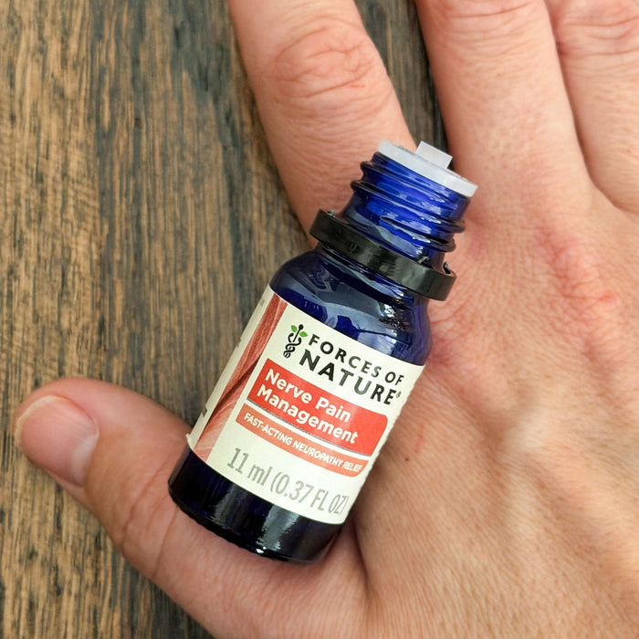 Angled view of Nerve Pain Management 11 ml blue glass bottle showcasing label text and dropper insert, held in a hand on a wood surface