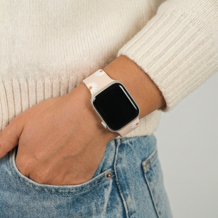 Neutral Daisies patterned Apple Watch strap on wrist, hand in light blue jeans pocket, cream sweater visible.