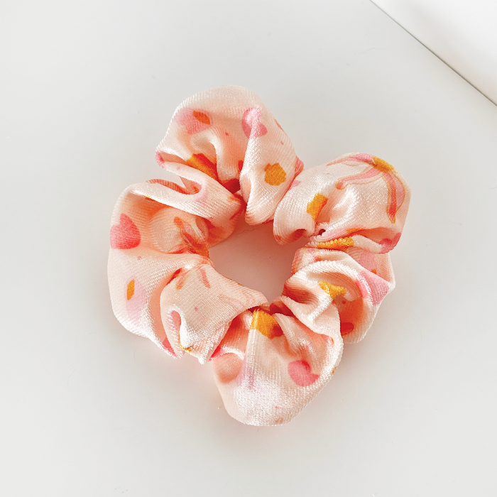 Pink satin scrunchie with orange and yellow abstract patterns on a white background.