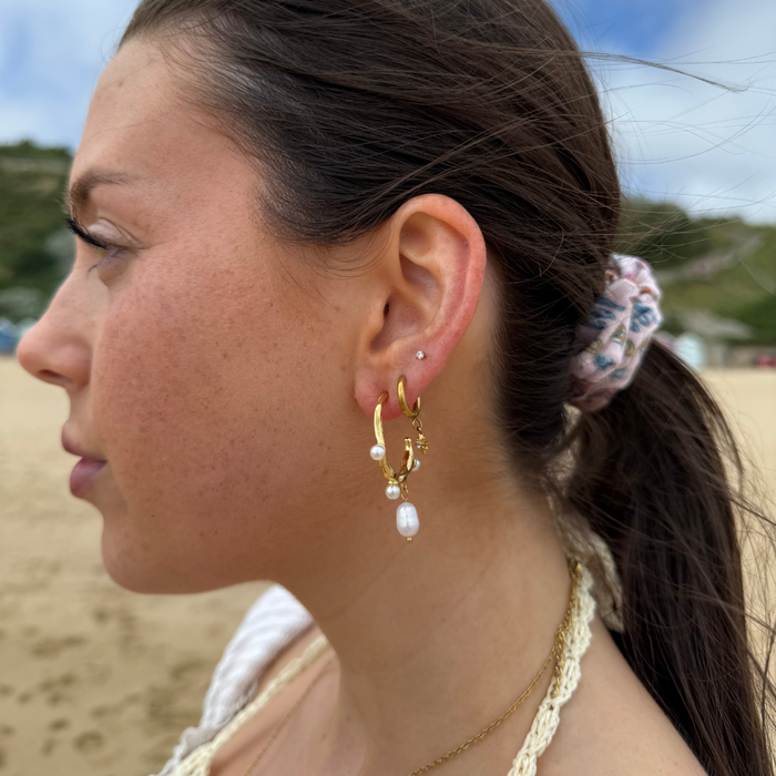 Woman with a ponytail wears pearl drop earrings by Coconut Lane while standing on a beach.