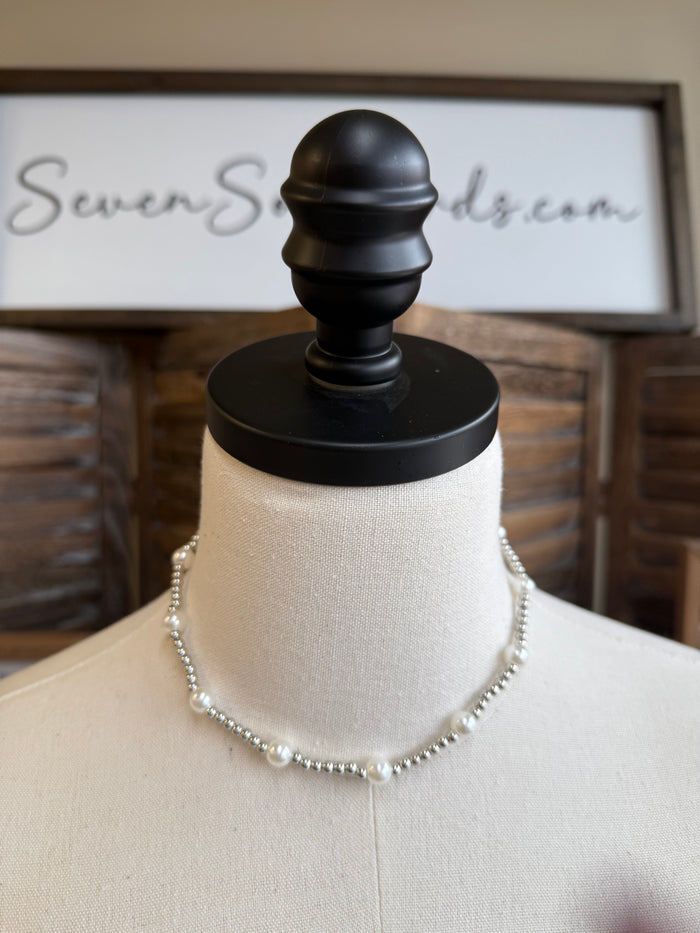 Pearl bead necklace with short chain and evenly spaced white pearls on mannequin