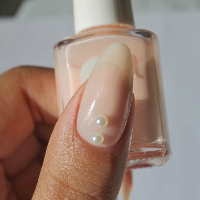 Pearly Whites pearl decals on a sheer nude nail, holding the bottle