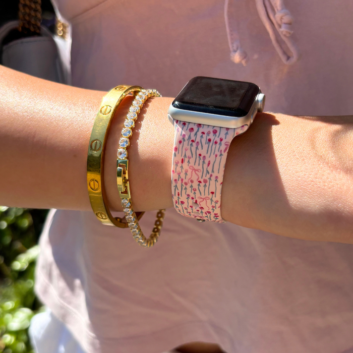 Wrist with Coconut Lane Peony Bow Apple Watch strap, gold bracelets, and a light pink top.