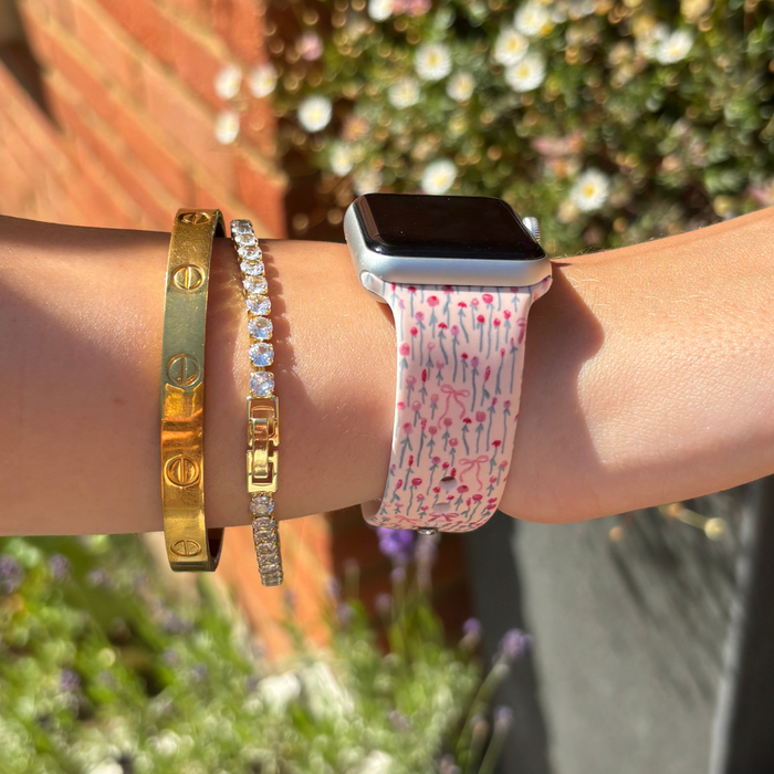 Wrist outdoors with gold and diamond bracelets and a pink floral Coconut Lane Peony Bow Apple Watch strap.