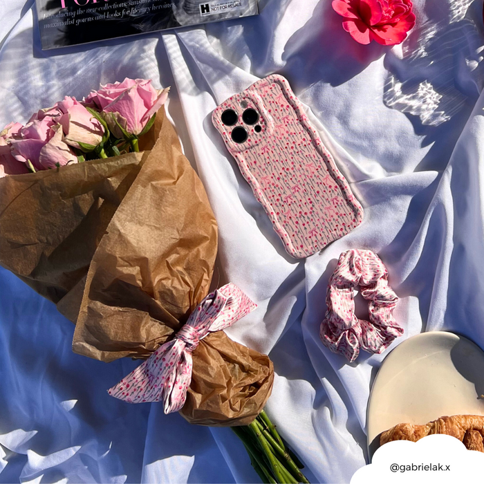 Pink bouquet, pink Peony Bow scrunchie, pink phone case, and pastry on white fabric in sunlight.