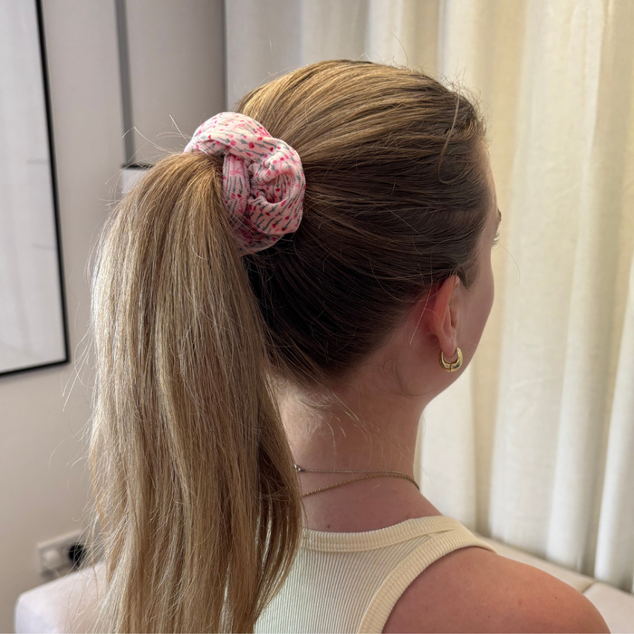 Blonde woman with a ponytail tied in a pink bow scrunchie, viewed from behind.