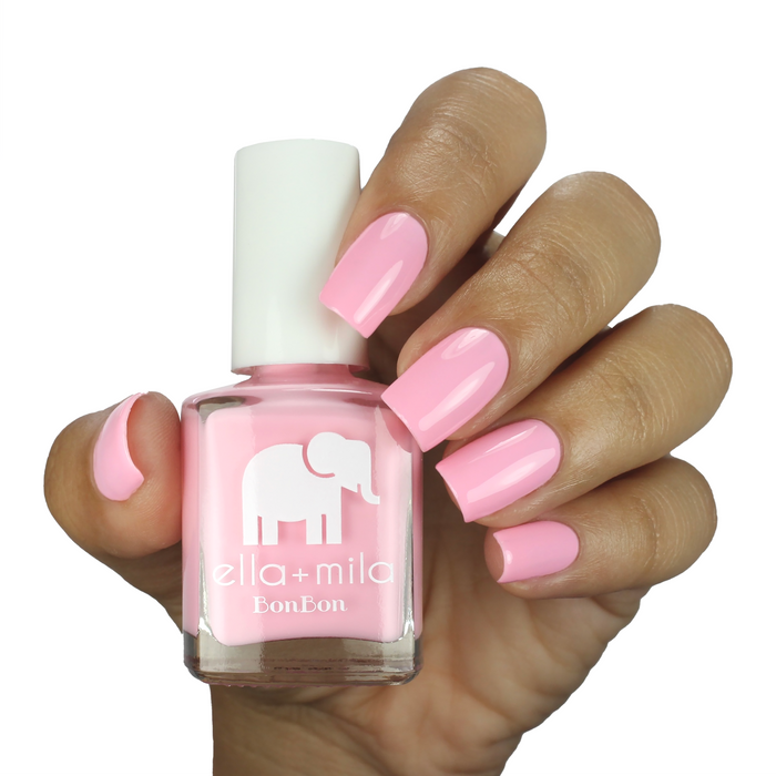 Pink Drink sweet light pink nail polish on a medium skin tone, hand holding the bottle