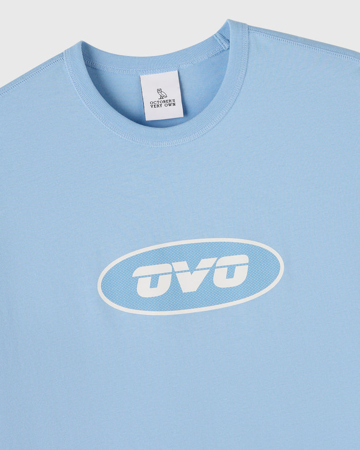 Light blue sleeveless muscle tee with white "OVO" oval logo print on chest and brand label at neckline.