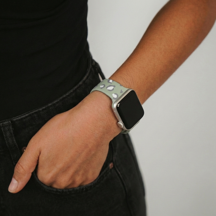 Sage green leopard print Apple Watch strap on wrist, hand in pocket of black jeans.