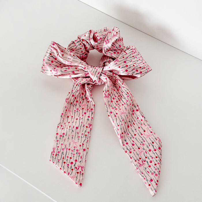 Pink satin bow scrunchie with long tails on a plain white background.