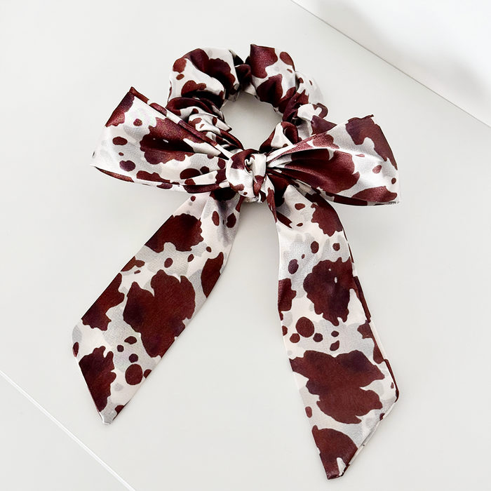 Satin scrunchie with large bow in black and white cow print pattern.