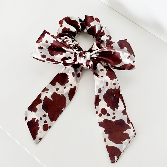Satin scrunchie with large bow in black and white cow print pattern.