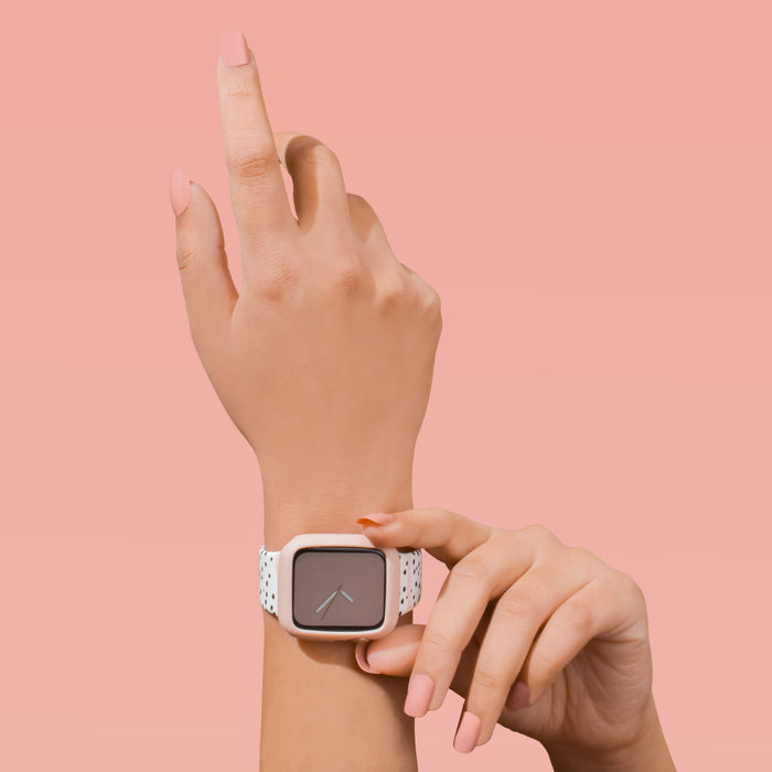 Coconut Lane pale pink silicone Apple Watch case worn by a person pointing upward, set against a pink background.