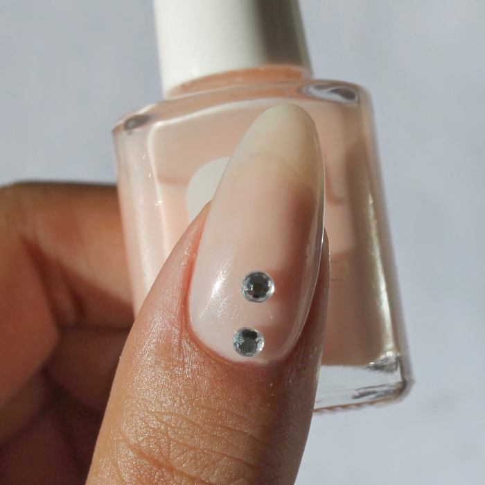 Silver Lining silver rhinestone decals on a sheer nude nail, holding the bottle
