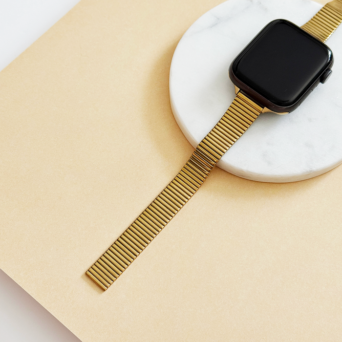 Gold SLIM Fine Line Apple Watch strap displayed on a round white marble tray against a beige background.