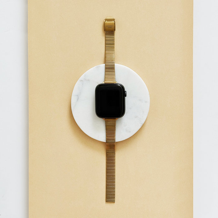 Gold Coconut Lane SLIM Fine Line Apple Watch strap displayed on a white marble disc with a beige background.